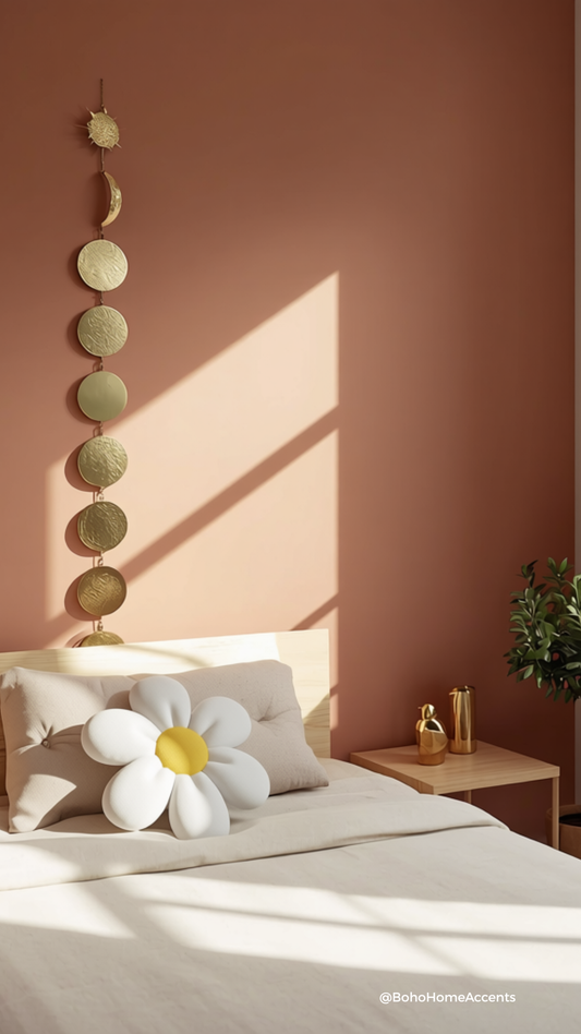 Modern bohemian bedroom featuring a soft pastel terracotta accent wall, styled with a gleaming vertical gold moon phase garland, an aesthetic plush white daisy flower pillow, and gold bird figurines under bright daylight.